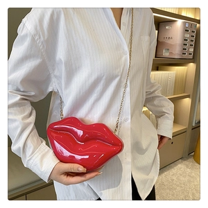Glossy red lip-shaped hard shell clutch bag with gold chain strap worn on person