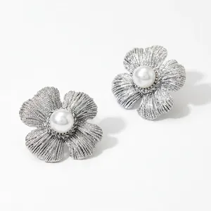 Gros plan sur des boucles d'oreilles fleur argentées avec pétales texturés et perle