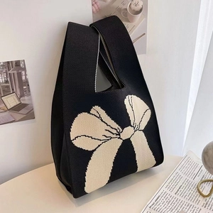 Close-up of a black knitted tote bag featuring a beige bow pattern in a minimalist setting