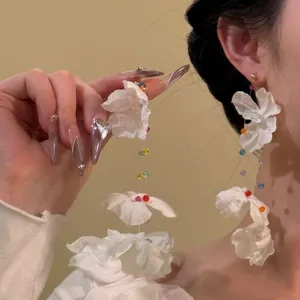 Gros plan de grandes boucles d'oreilles fleurs en organza blanc avec perles colorées