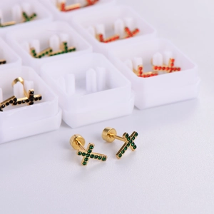 Close-up of gold cross stud earrings with green rhinestones and gift boxes