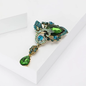 Detailed close-up of a vintage bronze brooch featuring emerald green and blue rhinestones