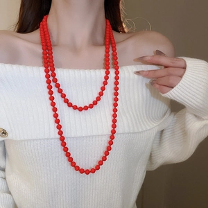 Detail of elegant double-layered long red pearl necklace styled on a white knitted sweater