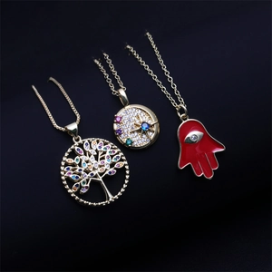 Three gold necklaces with tree of life, star, and red hamsa hand pendants on black background