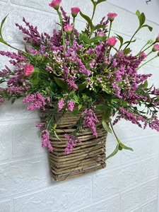 Close-up of rustic wicker wall basket with purple faux wildflowers and green leaves
