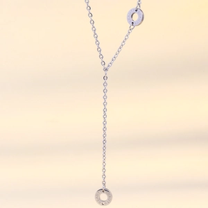 Dettaglio macro della collana a Y argento con anelli e incisione BEAUTY su sfondo beige