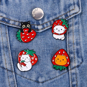 Macro detail of four strawberry cat enamel pins pinned on a blue denim jacket pocket