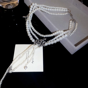 Détail du collier de perles triple couche avec nœud papillon et pendentif cœur