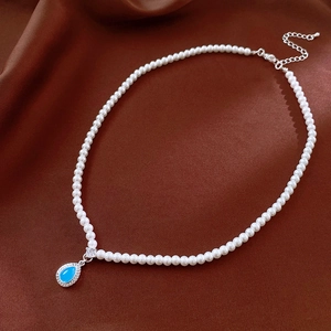 Close-up of pearl necklace with blue teardrop gemstone pendant on brown silk fabric