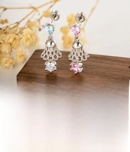Detail showing lace pendant earrings with pink and blue heart zircons on wooden surface