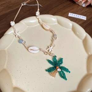 Detail der Perlenkette mit grünem Palmenanhänger und weißen Muscheln auf Keramikschale