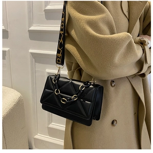 Detail of black quilted crossbody bag with designer wide strap and metal chain links