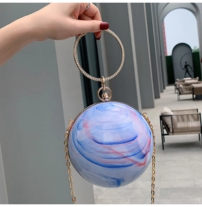 Detailed macro of a spherical acrylic evening bag with blue-pink marble texture and gold ring