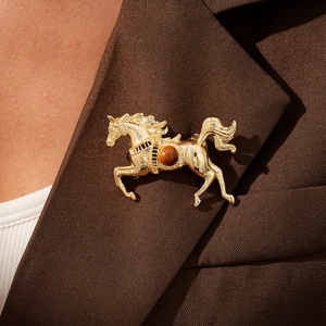 Close-up of a golden horse brooch with brown gemstone on a brown blazer lapel