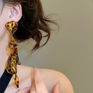 Close-up of long leopard print acrylic petal tassel earrings with a glossy amber texture