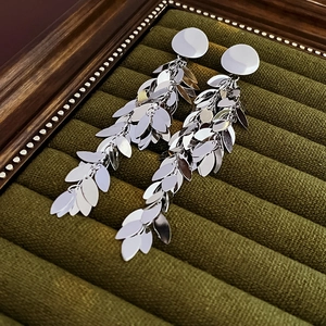 Detailed view of silver leaf tassel earrings hanging on a green velvet jewelry stand