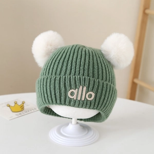 Detail der grünen Baby-Strickmütze mit zwei weißen Pompons und weichem Innenfutter