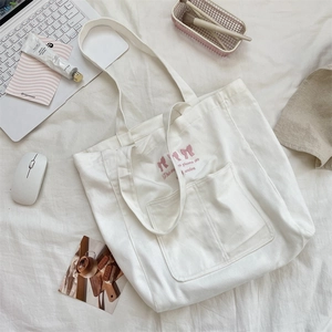 Detail of white canvas tote bag featuring embroidered pink bow and a front patch pocket