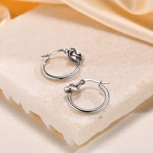 Detailed close-up of silver knot stud earrings on textured stone and silk background