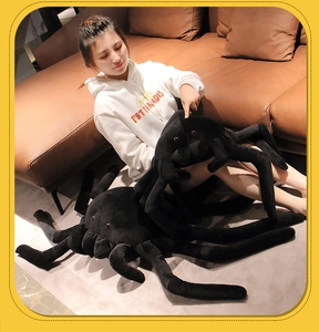 Detailed view of large black plush spider toys held in a cozy home setting with a sofa