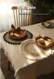 Detail of round jute placemat featuring white floral patterns and bohemian fringe edges