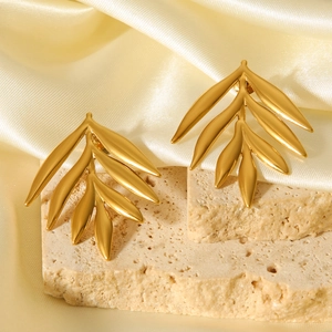 Macro shot of 18K gold leaf earrings on beige stone with golden silk background