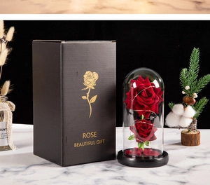 Preserved red roses in glass dome with LED lights beside a black gift box on marble surface