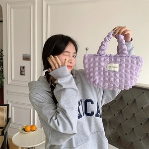 Detail of purple bubble texture fabric handbag held by model in home setting