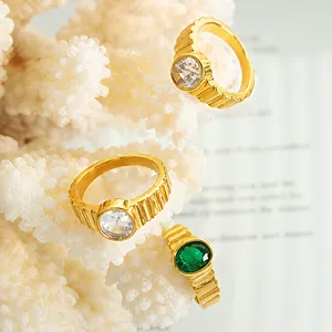 Detailed view of vintage gold-plated rings with green and clear zircon stones on a white coral