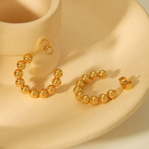 Macro detail of gold-toned titanium steel beaded C-shaped hoop earrings with butterfly back