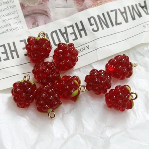 Macro detail of red resin raspberry charms with green leaves and gold hooks for DIY jewelry