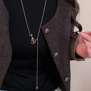 Detail of silver Y-shaped necklace with brown gemstone pendant on tweed blazer