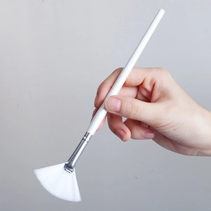 Close-up of a professional fan-shaped makeup brush with white bristles and wooden handle