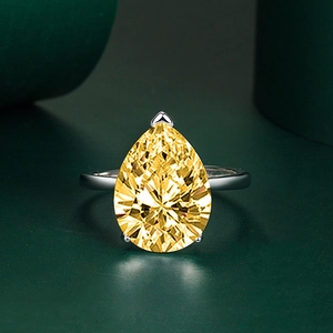 Macro shot of pear-cut yellow gemstone ring with silver band and three-prong setting