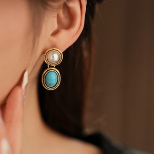 Close-up of vintage gold earrings featuring white pearl and turquoise stone on a model