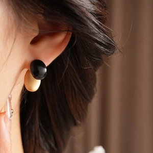 Close-up of minimalist black and gold oval earrings worn by a model in soft lighting