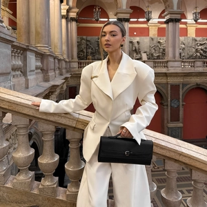 Women's cream white wide-shoulder blazer suit and wide-leg trousers in a classic architectural setting