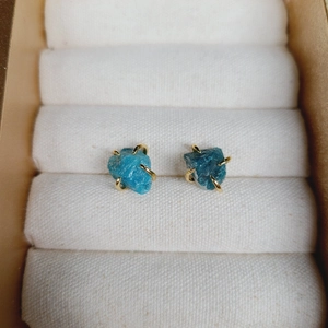 Detail of blue natural stone stud earrings with golden four-claw setting on display