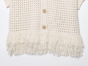 Detail of cream crochet knit top featuring round buttons and long bohemian tassel hem