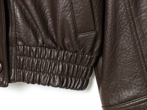 Macro shot of dark brown faux leather jacket detail showing hem and stitching