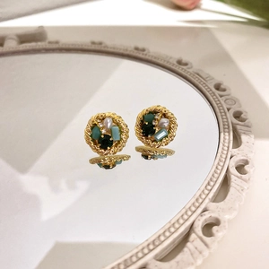 Detail of vintage gold-rimmed stud earrings with green gemstones and pearls on a mirror