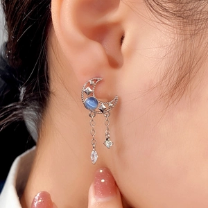 Elegant silver crescent moon earrings with blue gemstones and star tassels on a model