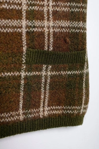 Close-up of brown and green plaid knit fabric showing wool texture and ribbed pocket detail