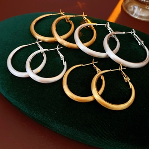 Close-up of four pairs of matte gold and silver geometric hoop earrings on green velvet