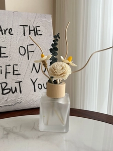 Close-up of frosted glass diffuser bottle with wood cap and dried botanical flowers