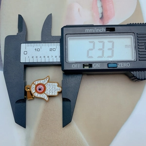 Macro shot showing golden Hamsa hand pendant dimensions at 23.3 mm with digital caliper