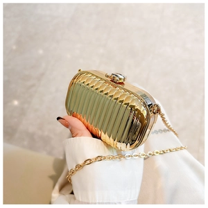 Close-up of golden metallic mini clutch bag with vertical pleat texture and thin chain