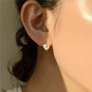 Close-up of a model wearing a gold heart stud earring with sparkling zircon crystal