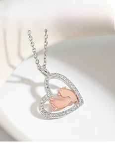 Close-up of heart pendant featuring rose gold baby footprints and pavé stone border