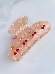 Detail of peach acetate hair claw clip with red cherry rhinestones on marble background